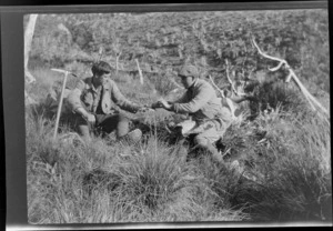 Edgar Williams, left and another man [Tracy Thomas Gough?], sitting among alpine grasses sharing a meal, Southern Alps, Canterbury Region
