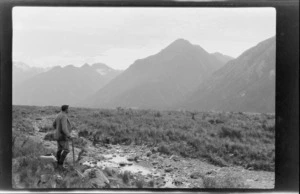 A man [Tracy Thomas Gough?] standing on a river plain, mountains beyond, Southern Alps, Canterbury Region