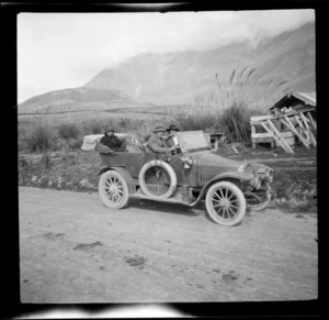 Motoring group, including Edgar Williams and Alice Hazlehurst, on an unsealed road next to a wooden agricultural structure, mountains beyond, Lake Coleridge, Selwyn District