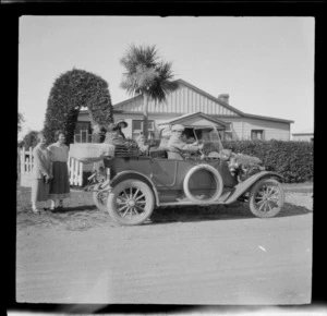 Motoring group, showing Edgar Williams behind wheel of a motorcar, with unidentified passengers and bystanders, parked in front of a wooden house with a topiary arch over front gate, [Peel Forest, Timaru District?]