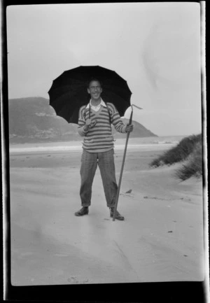 Owen Williams standing on a beach holding a hoe and an umbrella, Catlins District, Otago Region