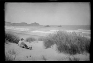 Alice Williams sitting on a sand dune overlooking sea and islets, Surat Bay, Catlins District, Otago
