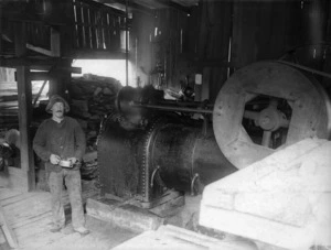 Man standing beside machinery in a timber mill, Akatarawa