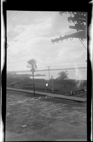 Public garden on waterfront with palm trees and street light, wharves beyond, location unidentified