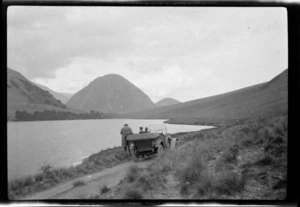 A motorcar parked on an unsealed road next to lake, [Canterbury Region?]