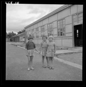 Three young girls pose outside the auditorium (sala odczytowa) at a Polish refugee camp, Pahiatua