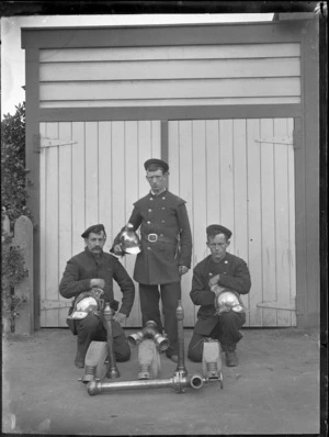 Three firemen in front of the Petone Fire-Brigade Station, with helmets, hoses and other pieces of equipment