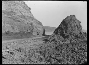 Lowry Bay Road, a narrow road between a hillside and a large rock on the foreshore.