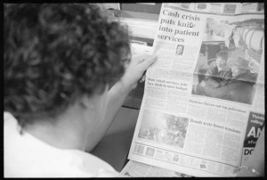 Woman reading a newspaper headlining cuts to patient services, New Zealand