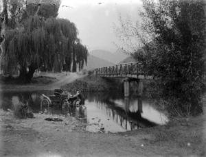 Scene at a ford, with a man pushing an Oldsmobile motorcar