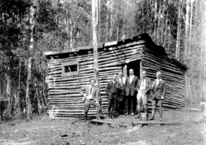 Men outside a log hut in the bush