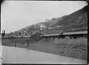 Men unloading spoil from railway trucks working with a ballast plough, on part of the reclamation at Kaiwharawhara, Wellington