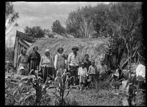 Maori family standing outside a whare thatched with palm fronds at Rangiahua, 1918.