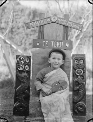 Albert Percy Godber's grandson Colin, seated beneath a carved sign for the Presbyterian Maori Mission at Te Teko.