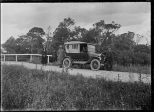 An automobile at Thompson's Bush (Mud Creek), Invercargill, with the photographer's wife and daughter (Laura and Phyllis Godber) standing on the left, and F Bonifant standing on the right
