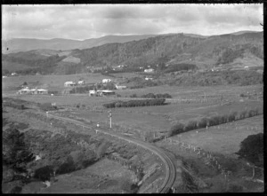 Landscape near Silverstream with railway track in the foreground, a few houses behind, and partially cleared hills in the background.