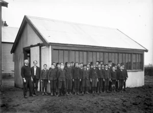 Group of school boys and two men outside a school building in Stratford