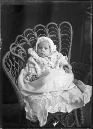 An unidentified infant seated in a cane chair