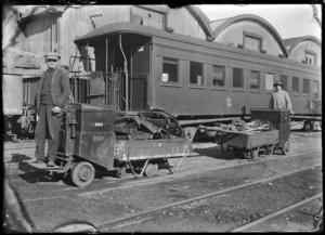Scene outside unidentified railway workshops, with two men with laden trolleys in front of a railway carriage