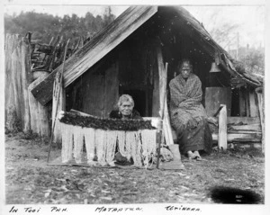 Maori women alongside a whare at Tooi Pa, Mataatua region