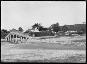 View of a footbridge over an inlet, with houses on the far side, probably at Raglan.
