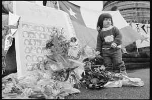 Ebie Monardez, 2, lays flowers beside a poster of the faces of some who disappeared during General Pinochet's rule in Chile - Photograph taken by Phil Reid