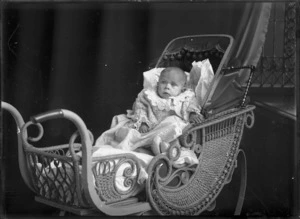 An unidentified infant seated in a cane pram