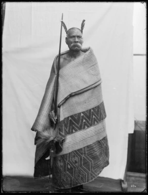 Unidentified Maori man wearing a cloak and holding a taiaha