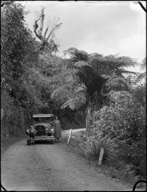 Motor car with Albert Percy Godber's wife, Laura Godber, and one of his grandsons standing in front of a car parked on a bend on the Akatarawa Road, circa late 1930s or early 1940s