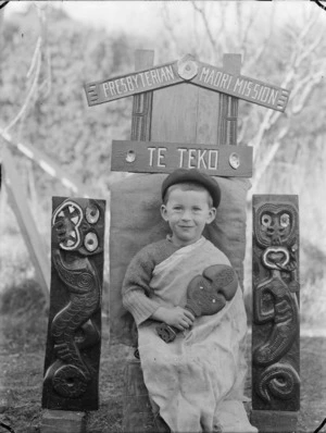 Albert Percy Godber's grandson Colin, seated beneath a carved sign for the Presbyterian Maori Mission at Te Teko.