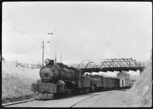 Steam locomotive hauling a goods train, passing beneath an overhead bridge.