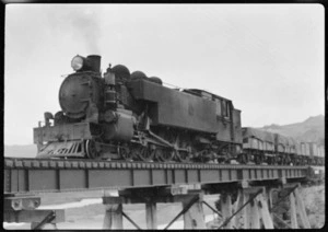 Steam locomotive hauling goods wagons, crossing an unidentified railway bridge