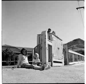 Children on a high locked cabinet at the entrance to a school, and, land clearance, in Wellington, 1974