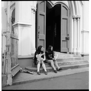 Two young women sitting on the steps of St. Peter's church in Willis Street, Wellington.