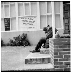 A man hunched over on the steps at the entrance to a church building