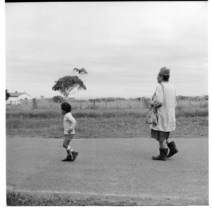 An older Māori woman walking along a road with a small boy wearing a caliper on his left leg, possibly in the Rotorua area