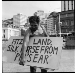 Māori man with a protest placard "Fitz's land. Silk purse from 'Pig's ear'"