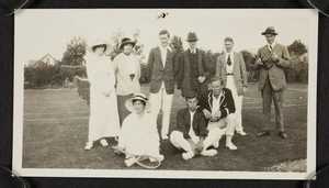 Group of men and women, some in tennis clothes, beside a tennis court