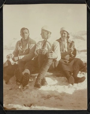 Two men and woman sitting in the snow eating, Switzerland