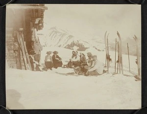 Group sitting in the snow beside a building, Switzerland