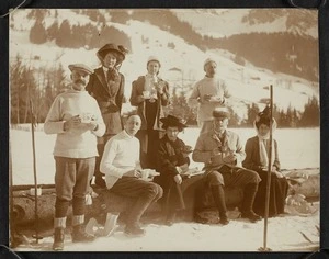 Group of men and women standing and sitting in the snow with food and tea cups.