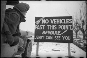 New Zealand jeep driver inspecting the sign erected in the NZ sector of the 8th Army front, Italy - Photograph taken by George Frederick Kaye
