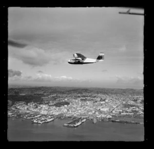 Tourist Air Travel, Grumman Widgeon aircraft in flight above Auckland Wharves and central city