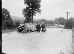 Men standing in flood waters near a partially submerged car