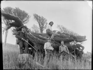Group of men with rifles and an axe around an orld totara log, near top of Mount Fitzgerald, Banks Peninsula, Canterbury