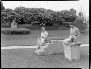 Two unidentified women sitting in a garden [outside a museum, Christchurch?] with exhibits of cannons and cannonballs