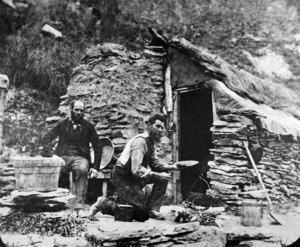 Two goldminers outside a hut