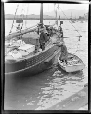 One man on a large sailing boat, possibly a fishing boat, while another man stands in a rowing boat beside it, location unidentified