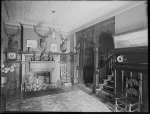 Lounge or hall of unidentified house, with deer head hunting trophies on the wall and other trophies on the mantelpiece