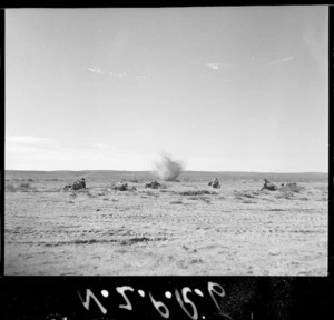 Open desert in the Sirte area, Libya, during World War 2, showing an enemy mortar exploding in front of advancing New Zealand soldiers
